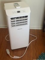 Front view of portable air conditioner with remote on top and power cord visible