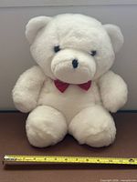 Front view of white plush polar bear with measuring tape showing width