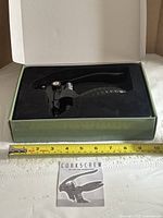 Corkscrew in open box with instruction leaflet and tape measure for scale