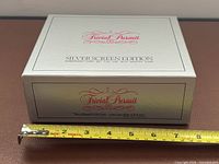 Closed silver outer box with Trivial Pursuit logo and tape measure for scale