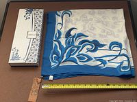 Scarf spread out next to presentation box with measuring tape for scale