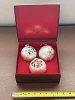 Three ornaments in open red-lined case with ruler for scale