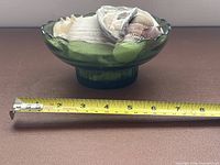 side view of green glass bowl filled with shells with tape measure showing length