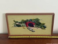 Front view of framed needlepoint showing full artwork and measuring tape for scale