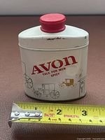 Front of tin showing logo, graphics, red cap, dent, tape measure indicating size