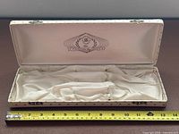 Open case showing satin interior and logo, tape measure for scale