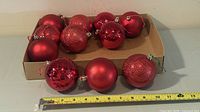 All eleven red ornaments in shallow tray with measuring tape showing roughly 3 in diameter