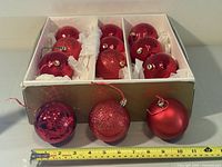 Box containing 12 red ornaments with three removed and tape measure showing size