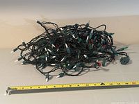 Coiled green-wired mini light string beside measuring tape for length reference