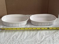Top view of both white oval dishes beside measuring tape showing length approx. 8 in