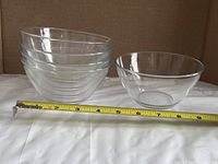 Stack of four clear glass bowls with separate single bowl, tape for scale