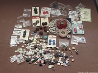 Overview of entire lot spread on surface: loose buttons, button cards, pin cushion, trim, thimble, bias tape, bobbin, needle threaders