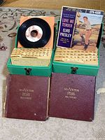 Two open green storage boxes containing 45 rpm records with Elvis Presley EP on top and numbered dividers; two RCA Victor binders beneath