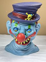 Front three-quarter view of blue clown bust with purple hat and red nose
