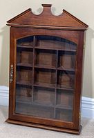 Front view of brown wood wall cabinet with glass door and pediment