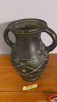 Front view of dark green/black amphora-style ceramic vase with double handles