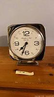 Front view of chrome square mantel clock on base, white dial visible