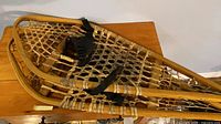Pair of wooden snowshoes stacked showing frames, webbing, bindings