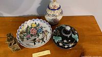 Group shot of ginger jar, plate, black lidded bowl, and carved seal on table