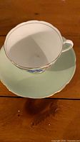 Teacup on saucer showing exterior mint green glaze, floral band and gold trim