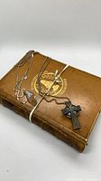 Necklaces and book arranged; shows crystal pendant necklace, Celtic cross necklace and vintage brown leather hardcover book