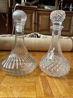 Both clear glass decanters showing patterns and stoppers