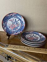Stack of four Imari-style plates with ruler showing diameter and one plate on stand