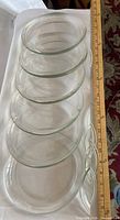 Six stacked clear glass dessert plates with ruler showing diameter