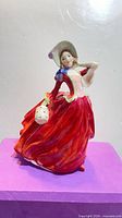 Front view of Royal Doulton Autumn Breezes figurine showing flowing red dress, bonnet and muff