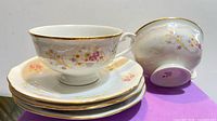 Stack of three saucers with teacup on top and second teacup on side showing pattern and gold rim