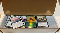 Open cardboard card box showing large quantity of Magic: The Gathering cards with various colors and a foil card on top