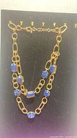Front view of gold-tone double chain necklace with blue stones on display board