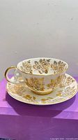 Teacup on saucer front view showing gold rose pattern and gilded handle