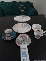 Group view of two teacup/saucer sets, creamer, dessert stand