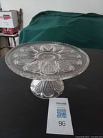 Full view of clear pressed glass pedestal cake stand on black surface