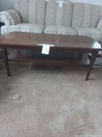 Rectangular cherry wood coffee table with lower shelf shown on carpeted floor
