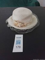 Top view of cream ladies hat showing brim, crown, flower band and veil