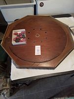 Octagonal crokinole board with box of discs on playing surface, showing wear and missing two discs