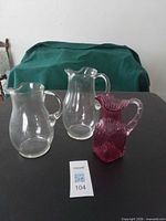 Three jugs grouped: two clear, one pink pressed glass