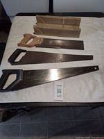 All four items laid out on towel: two panel saws, one back saw, one mitre box