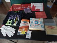 All cloth items laid out on table: T-shirt, gloves, mittens, two flags, bandana, dish cloth, chiffon wipes pack, cheesecloth pack, magic towels