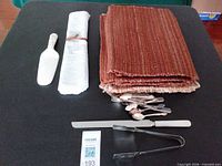 All items laid out on table: placemats, rolled cloth, teaspoons, cake server, spreader, tongs