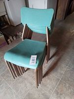 Stack of blue plastic chairs with bronze metal legs, lot tag visible