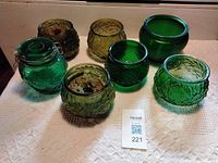 Seven textured green and amber glass containers on cloth