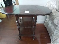 Full view of wooden drop-leaf tea trolley showing two tiers, turned legs, casters