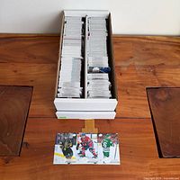 Open white two-row card storage box filled with loose hockey trading cards; three sample cards displayed in foreground