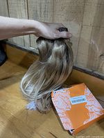 Hand holding bundle of light brown/ash blonde clip-in extensions beside orange Full Shine box