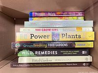 Stack of nine paperback gardening and remedy books inside carton