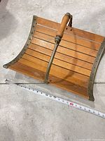 Top view showing slatted wood surface, arched metal handle, metal edge trim, measuring tape indicating width