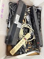 Top view of box showing multiple APC and Belkin rack PDUs, beige 6-outlet strip, cords